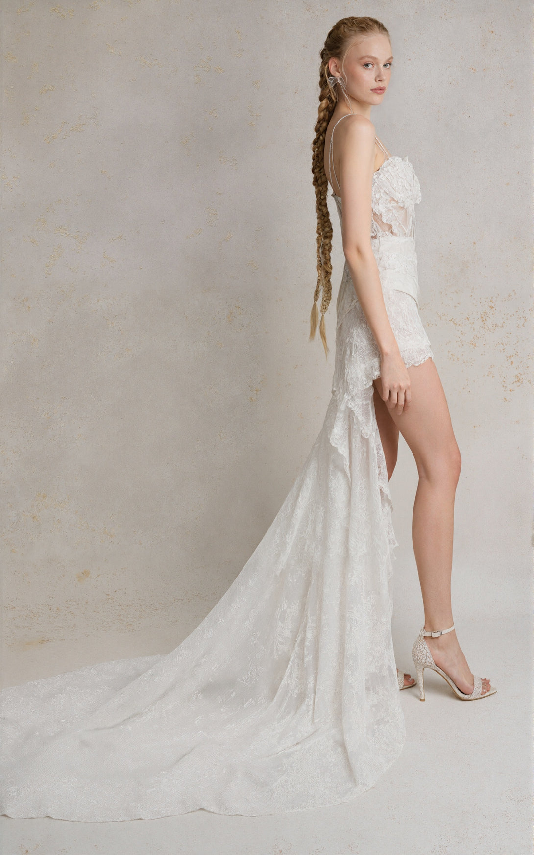 Woman wearing a white lace wedding dress with a high slit on a plain background