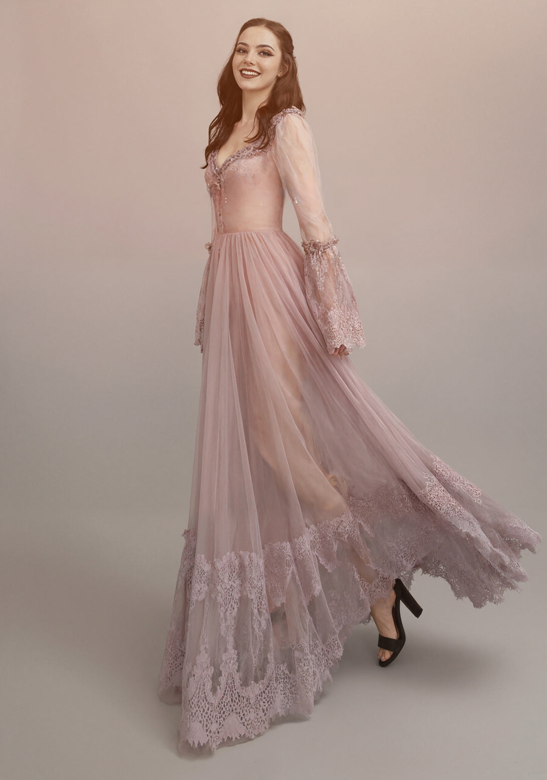 Woman wearing a long, lace-trimmed dress against a plain background