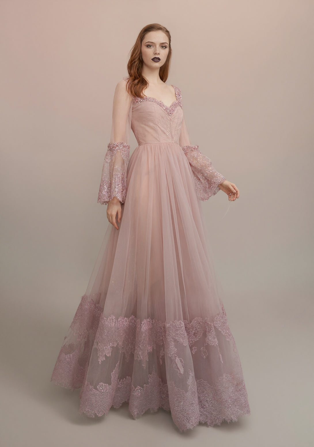 Woman wearing a pink lace evening gown against a neutral background