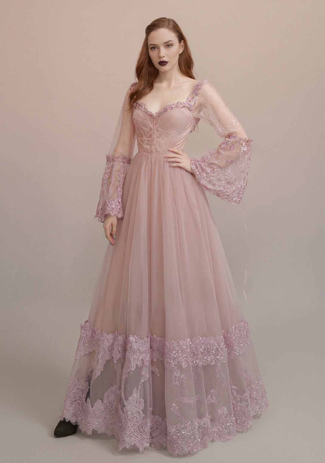 Woman wearing a pink evening gown with lace details on a beige background